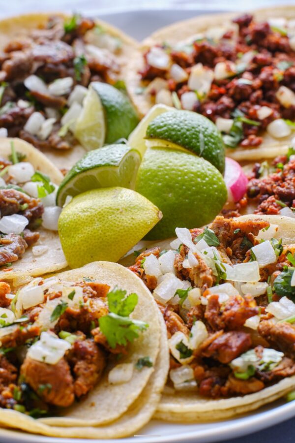 Overhead image of a variety of tacos on a plate with limes in the middle