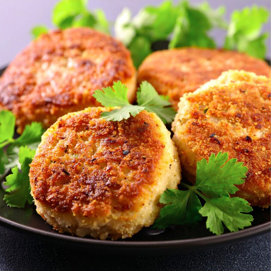 Four crab cakes on a plate with parsley