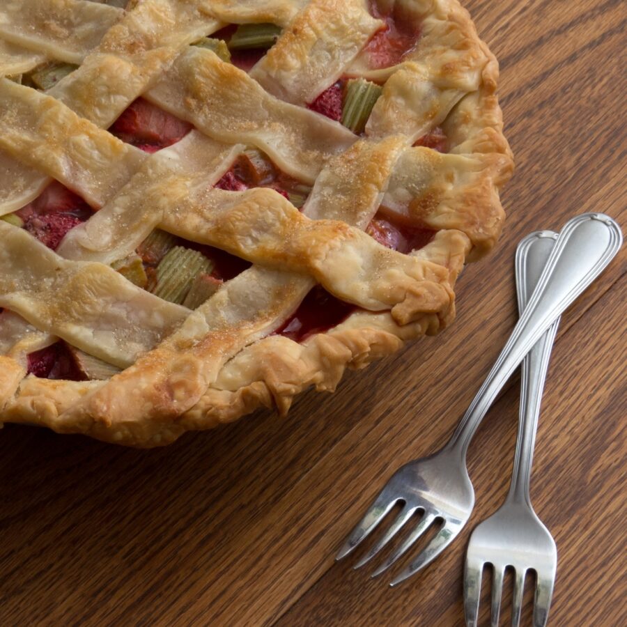 Close up image of a rhubarab pie with a lattice top with two forks sitting next to it