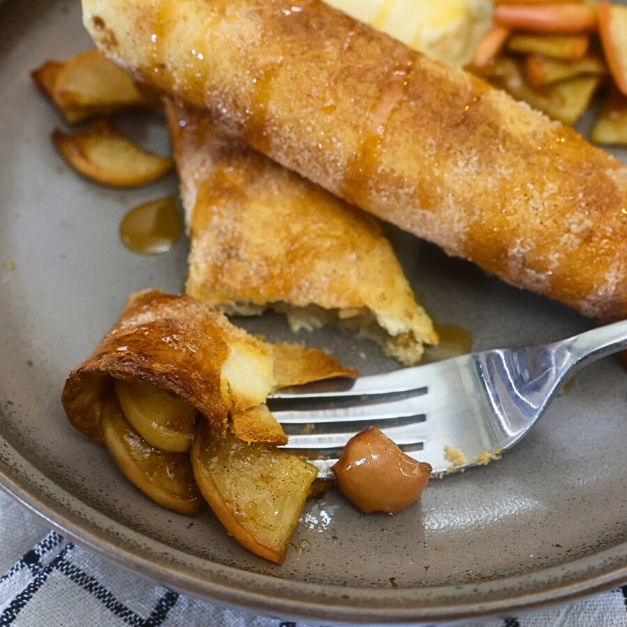 Two air fryer apple pie taquitos with a bite cut off of the end of one