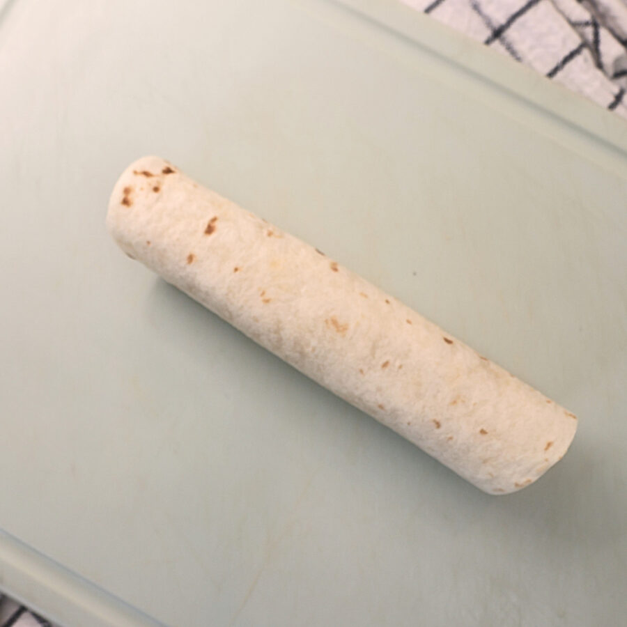 Rolled uncooked apple pie taquito on a cutting board