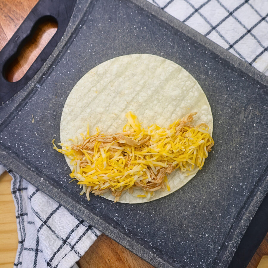 A corn tortilla on a cutting board filled with seasoned cooked chicken and cheese