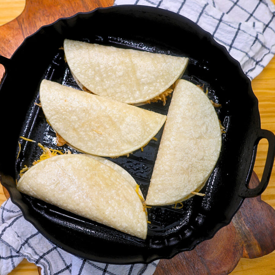 Four chicken and cheese tacos with corn tortillas in an air fryer basket