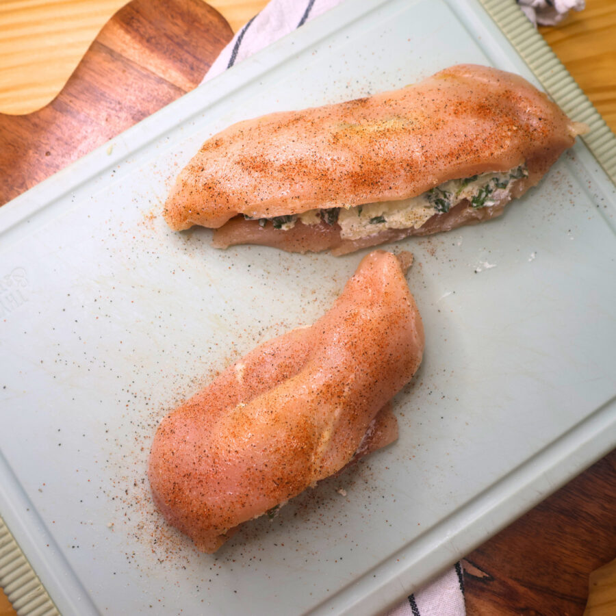 Two stuffed chicken breasts seasoned on a cutting board