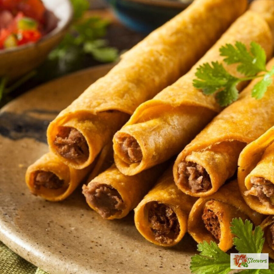 CLose up image of air fryer taquitos stacked on a plate with cilantro and salsa in the background