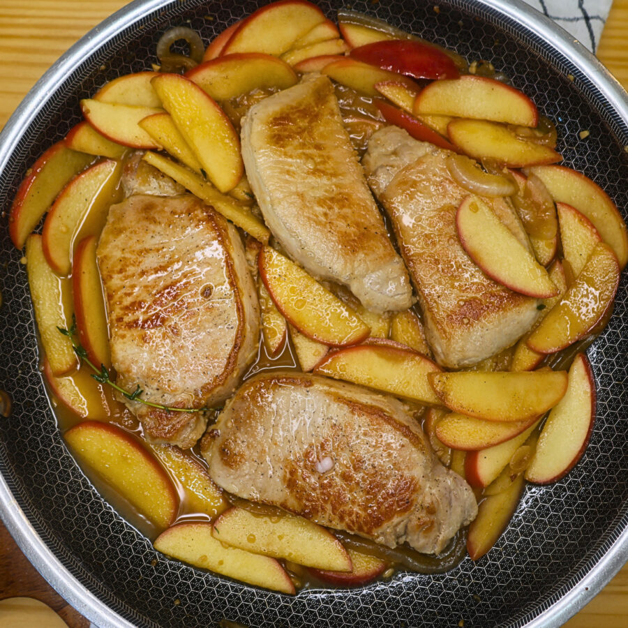 Cooked apples and sliced onions in a skillet wi th seared pork chops