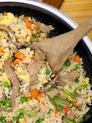Close up image of beef fried rice in a skillet with a wooden spoon