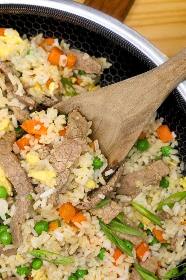 Close up image of beef fried rice in a skillet with a wooden spoon