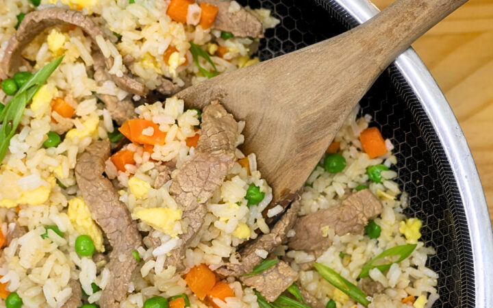 Close up image of beef fried rice in a skillet with a wooden spoon