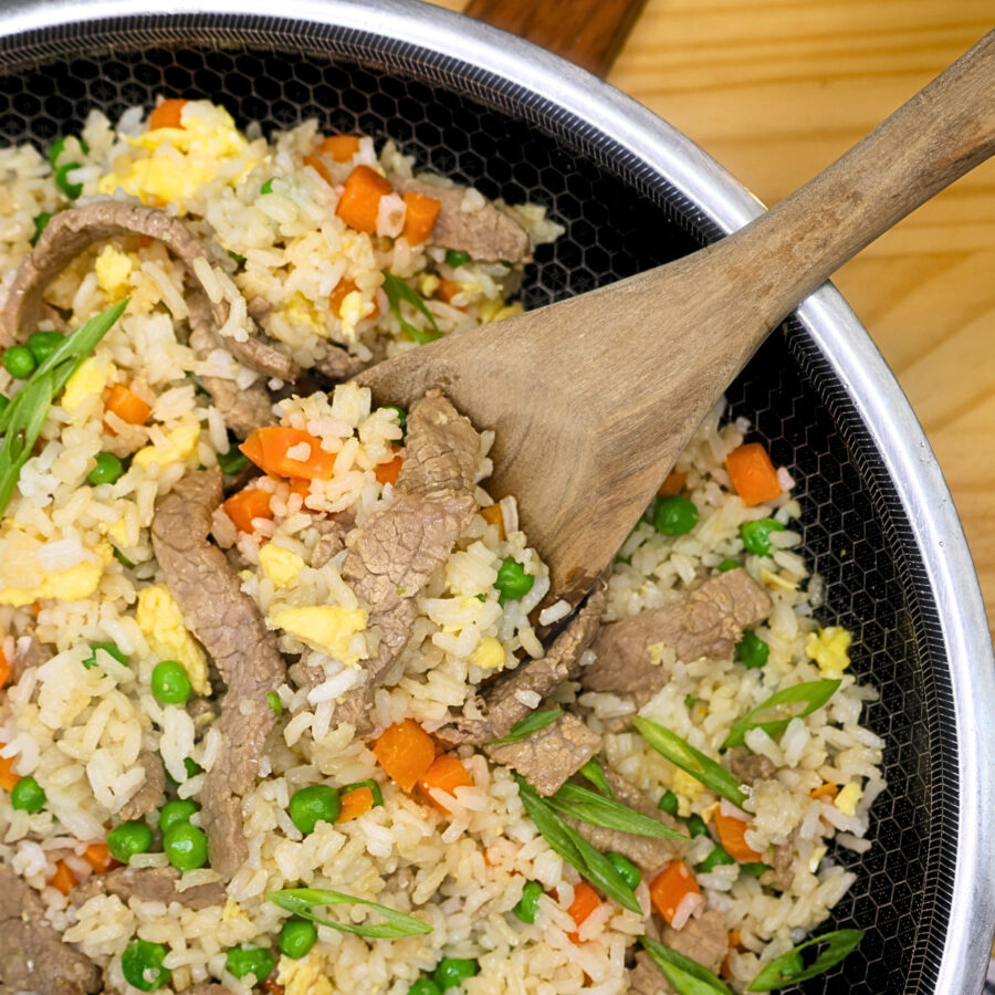 Close up image of beef fried rice in a skillet with a wooden spoon