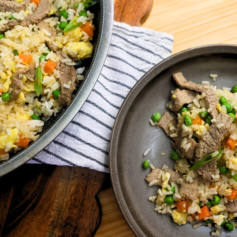 A serving of beef fried rice on a plate next to a full skillet