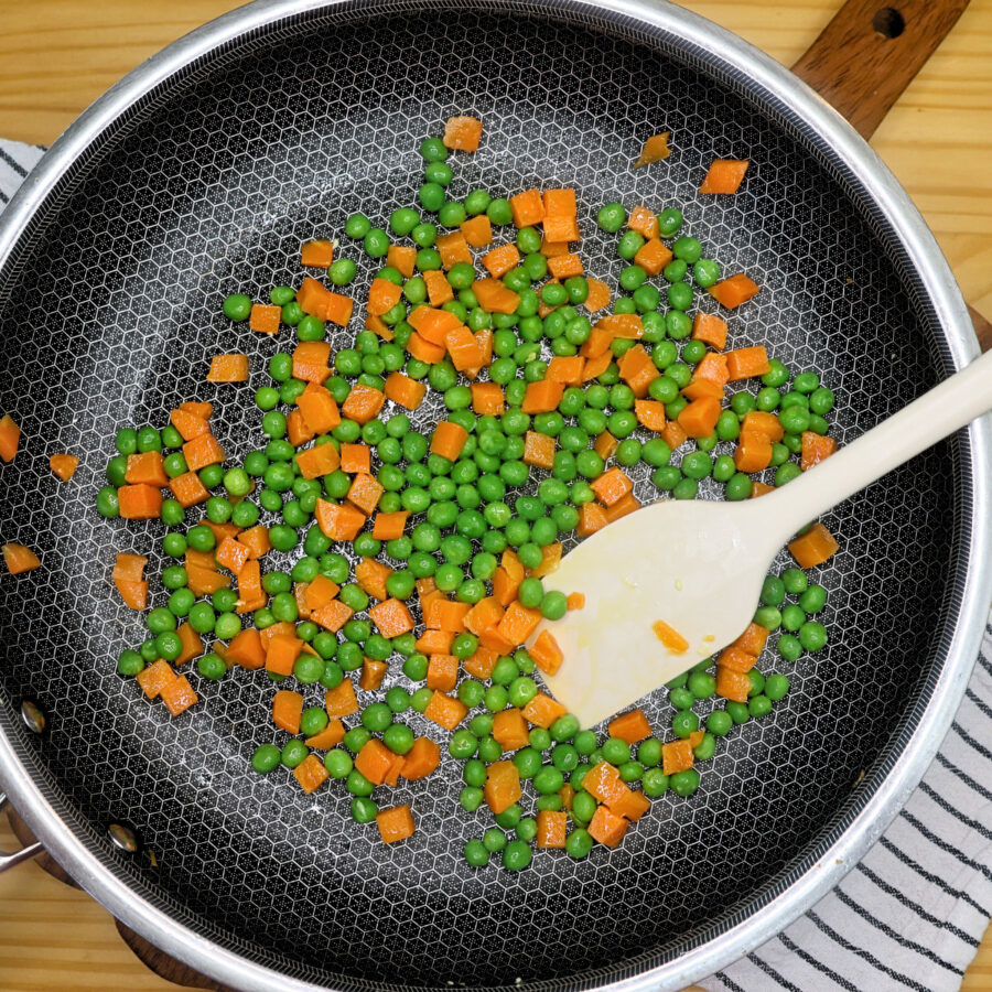 diced carrots and peas cooking in a skillet