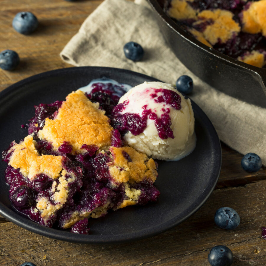 A serving of blueberry cobbler on a plate with ice cream