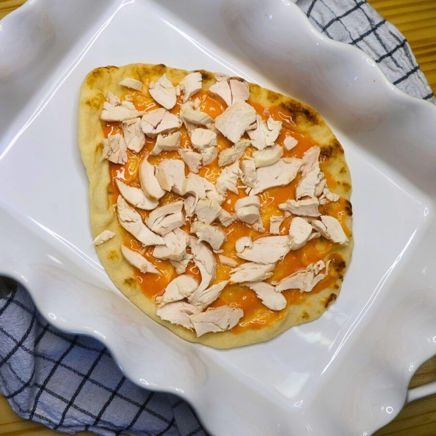 A large flatbread with buffalo sauce and shredded chicken in a white baking dish