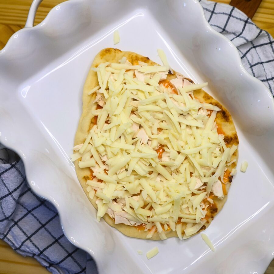 Flatbread in a pan with buffalo sauce, shredded chicken, and cheese
