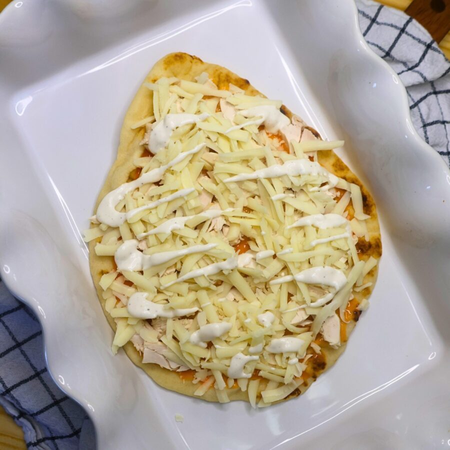 Unbaked buffalo chicken flatbread in a white baking dish