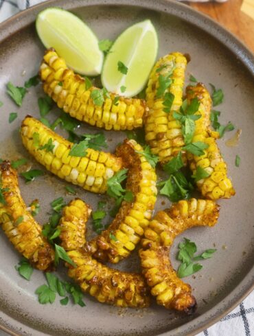 Overhead image of Cajun Butter Corn Ribs with parsley and lime wedges