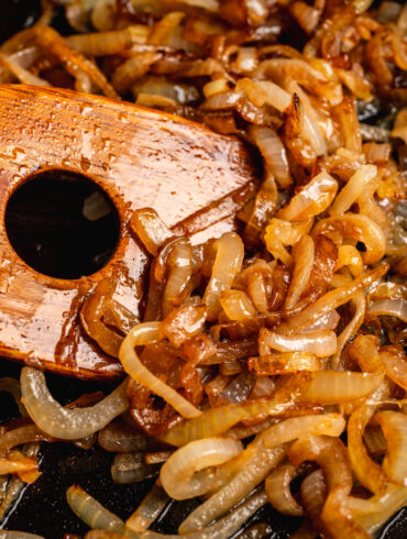 Close up image of caramelized onions being stirred with a wooden spatula