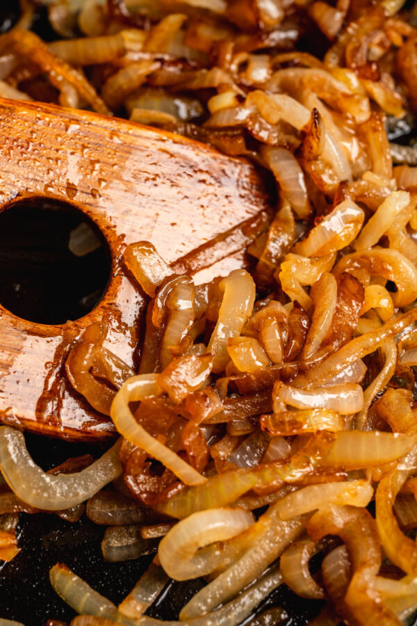 Close up image of caramelized onions being stirred with a wooden spatula