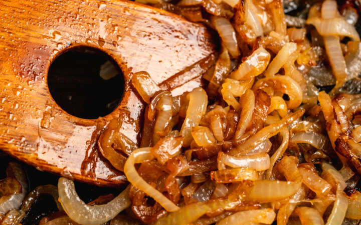 Close up image of caramelized onions being stirred with a wooden spatula