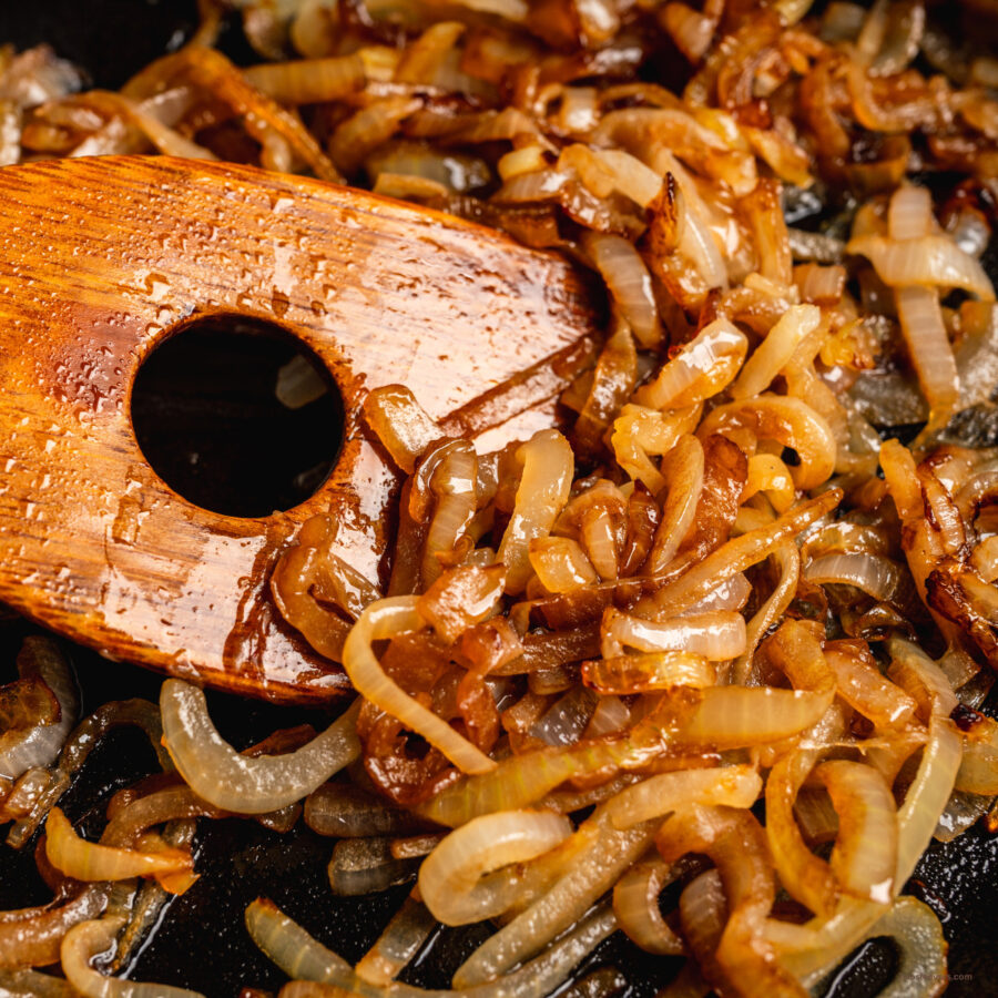 Close up image of caramelized onions being stirred with a wooden spatula