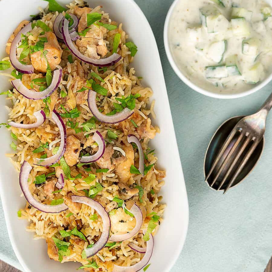 Overhead image of Instant Pot Chicken Biryani with raita and silverware