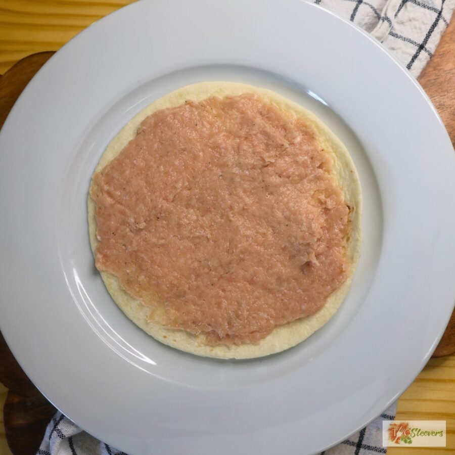 Uncooked ground chicken spread on a flour tortilla