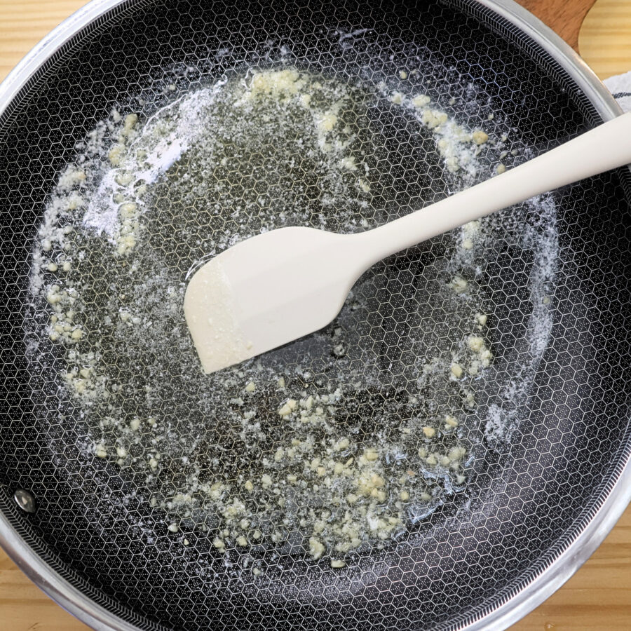 A skillet with melted butter and garlic being cooked with a silicone spatula