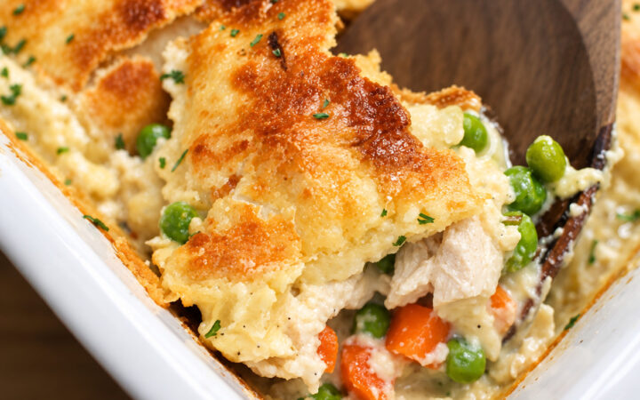 Close up image of chicken pot pie casserole being served with a wooden spoon