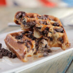 A homemade chocolate chip waffle cut in half on a plate