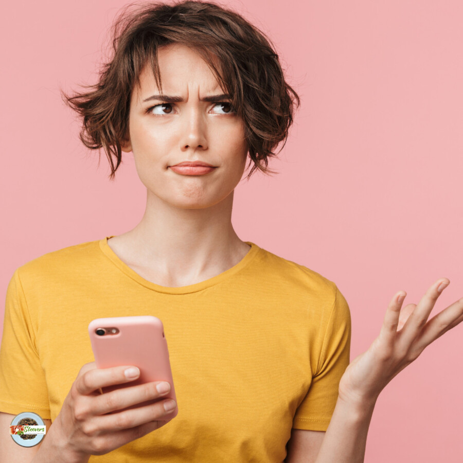 A woman in a yellow shirt holding a phone looking confused