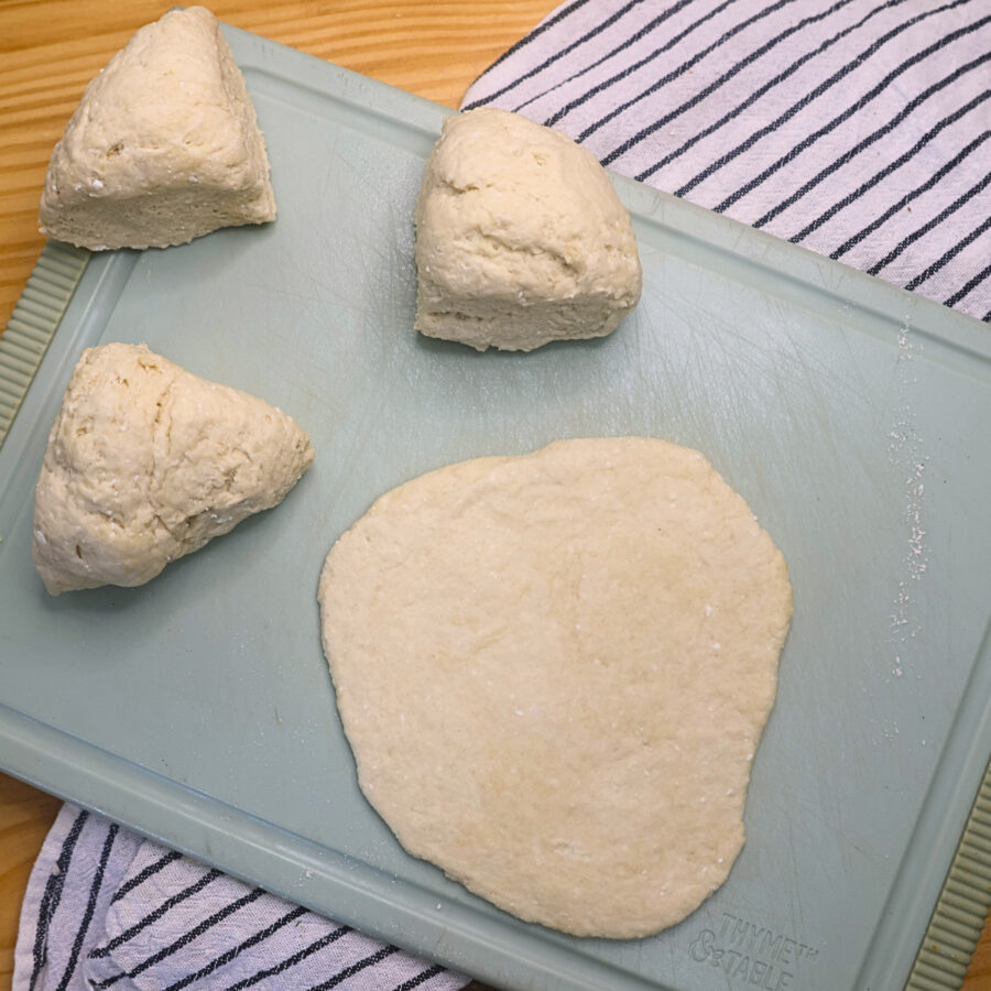 Cottage cheese flatbread dough divided into four pieces with one rolled out