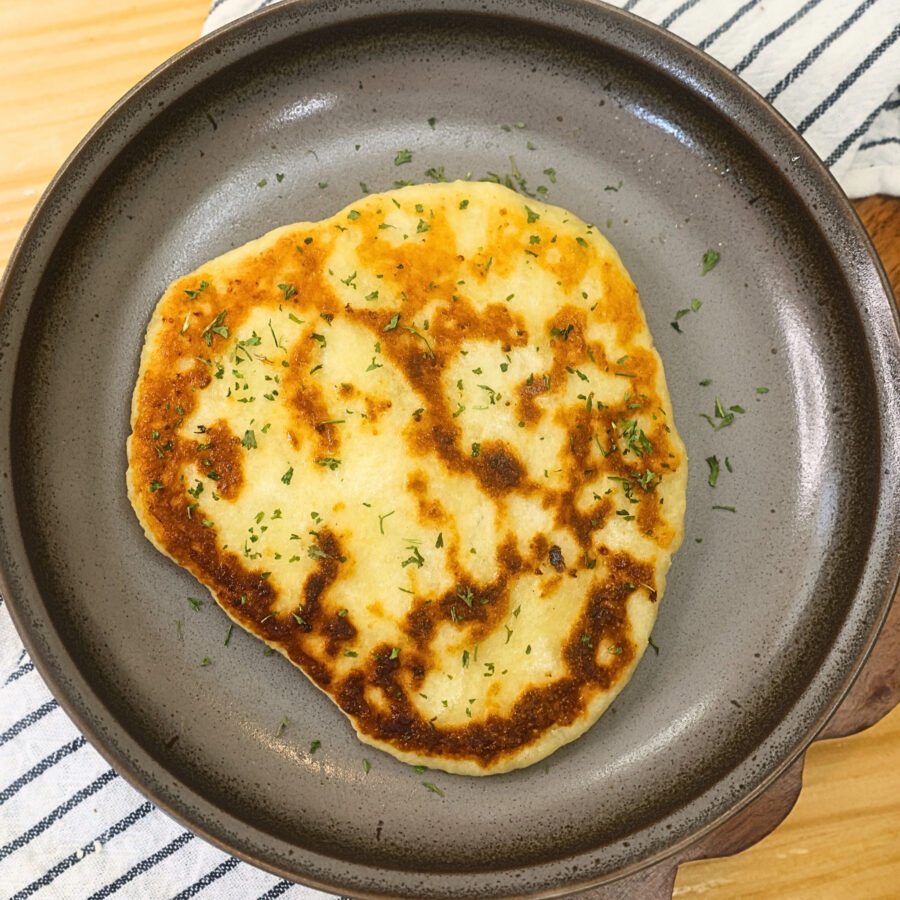 Cooked flatbread on a plate coated in olive oil and herbs
