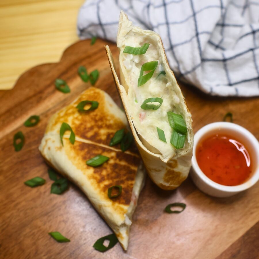 Overhead image of a crab rangoon burrito cut in half on a wooden serving tray with dipping sauce