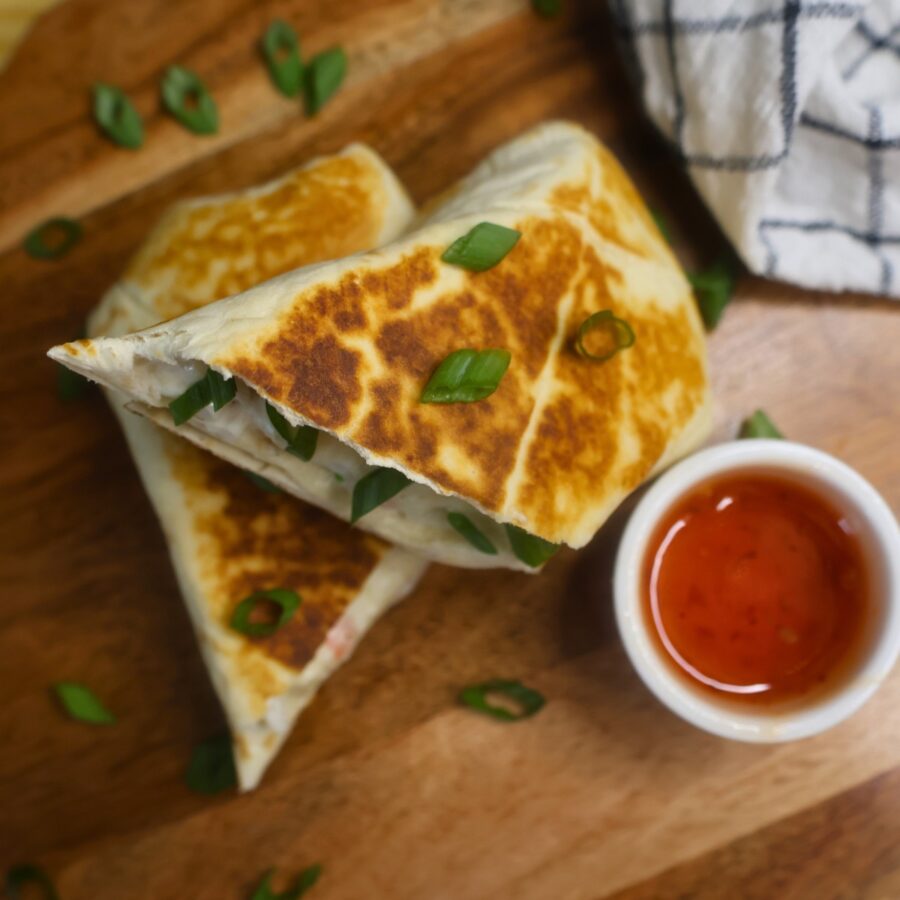Overhead image of a toasted crab rangoon burrito cut in half with a small bowl of sweet chili sauce