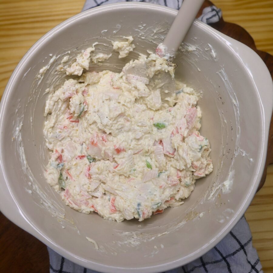 Filling for a crab rangoon burrito in a mixing bowl with a silicone spatula