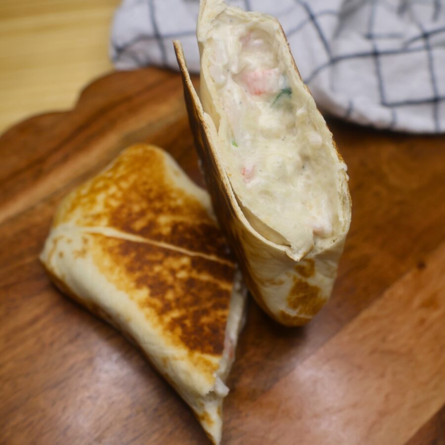 A toasted crab rangoon burrito cut in half on a wooden serving tray