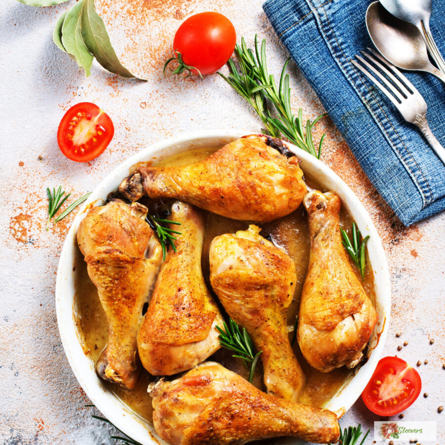 Crispy Baked Chicken Legs in a white dish surrounded by rosemary and cherry tomatoes