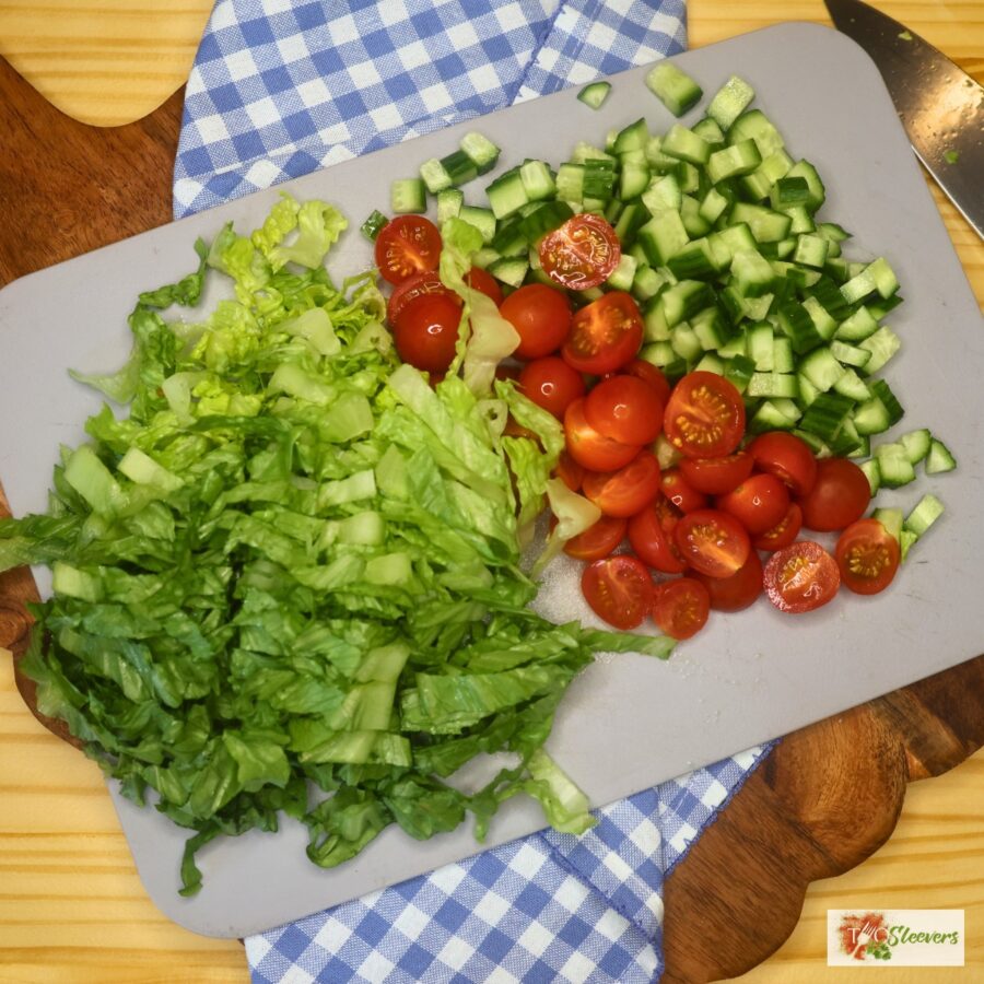 Chopped lettuce, cucumber, and cherry tomato on a cutting board