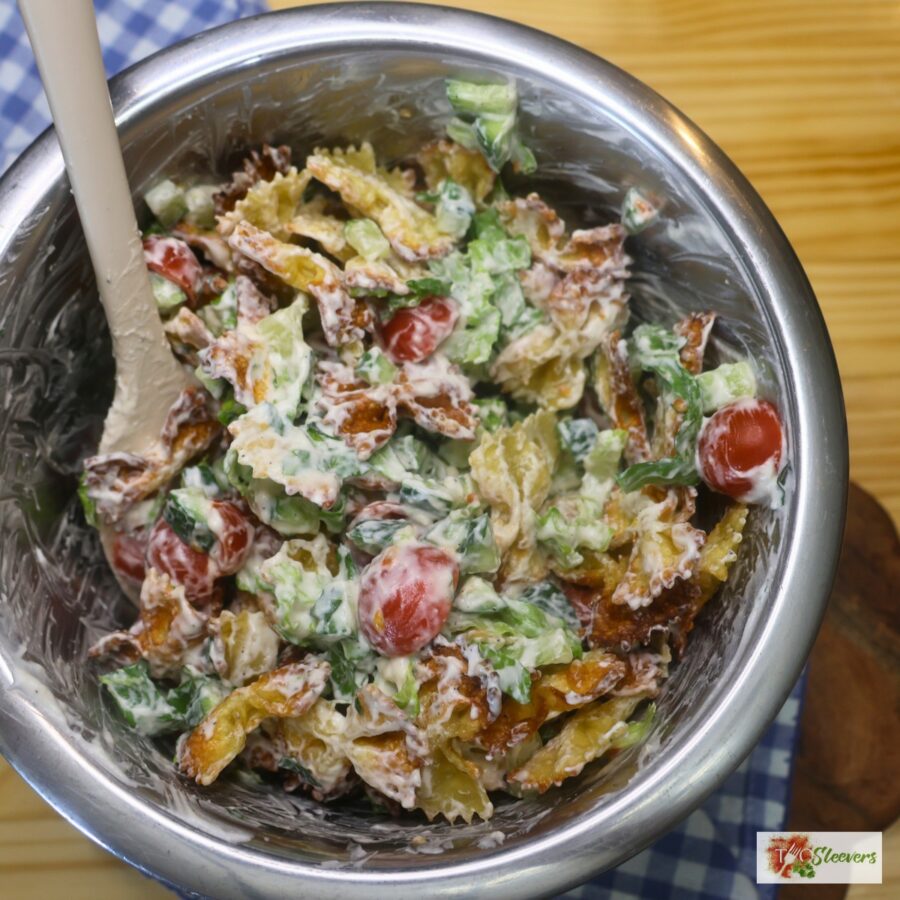 Crispy pasta salad being tossed in a bowl with a silicone spatula