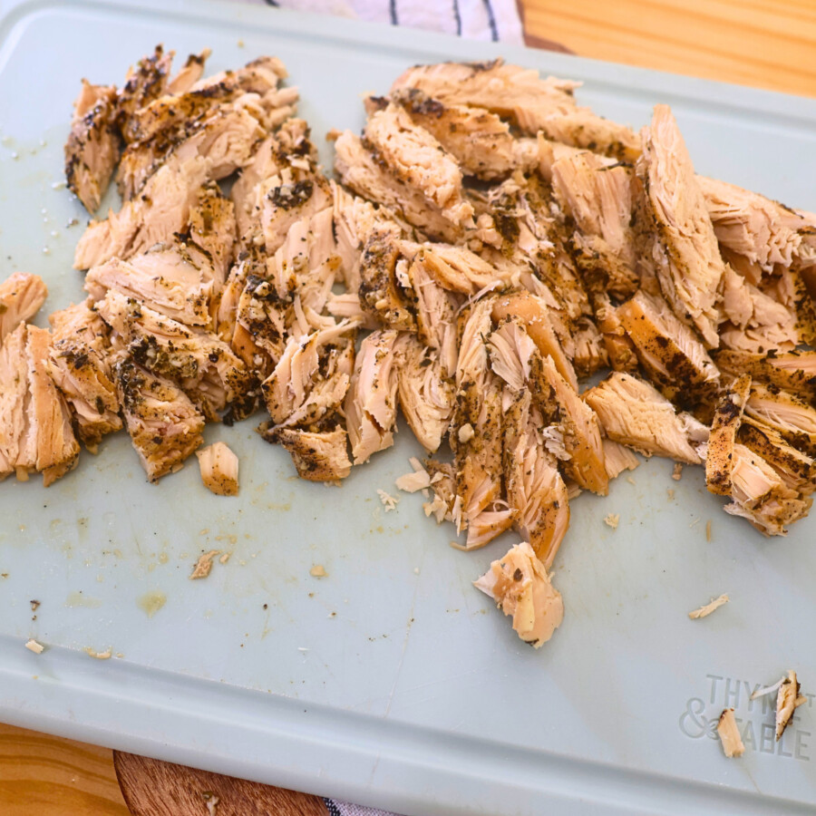 Chicken breasts that were cooked in the crock pot diced on a blue cutting board