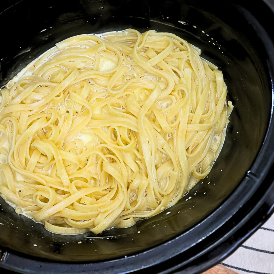 Homemade alfredo sauce and cooked fettuccine noodles in a crockpot