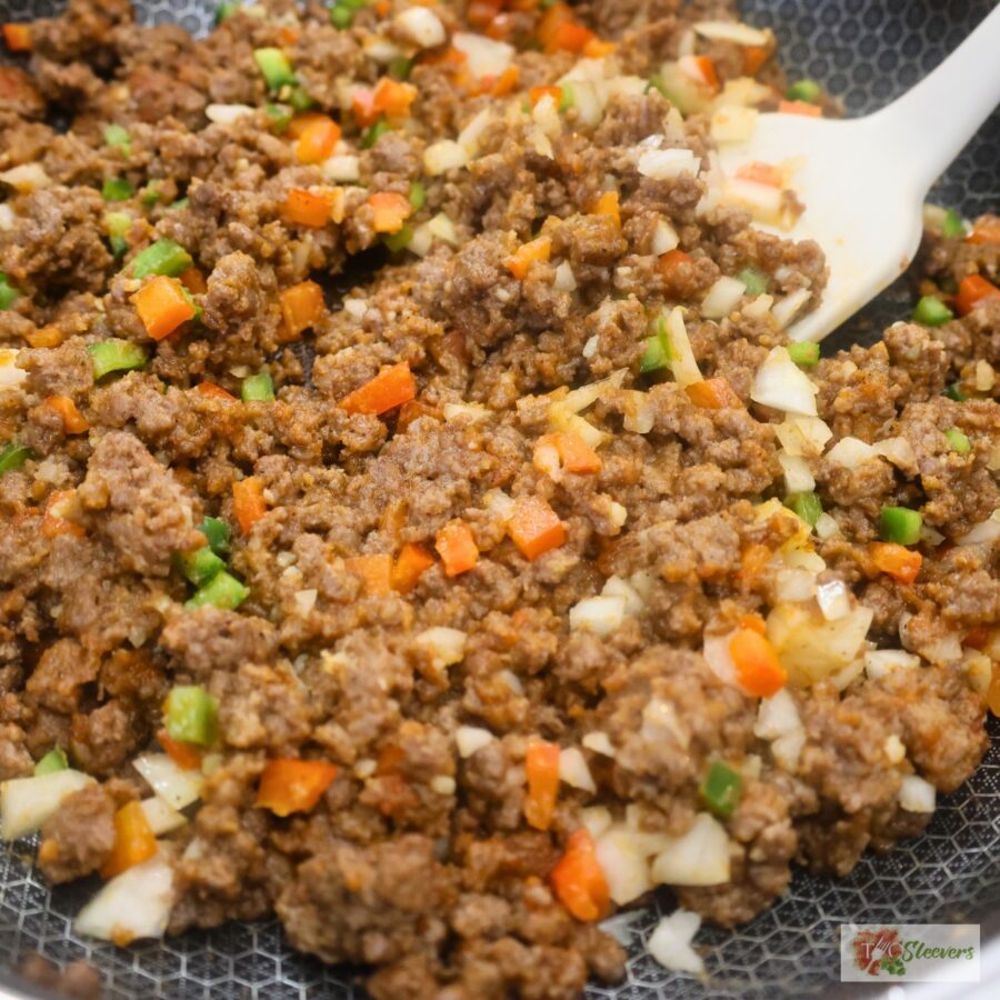 Close up image of seasoned ground beef with cooked onions and peppers in a skillet