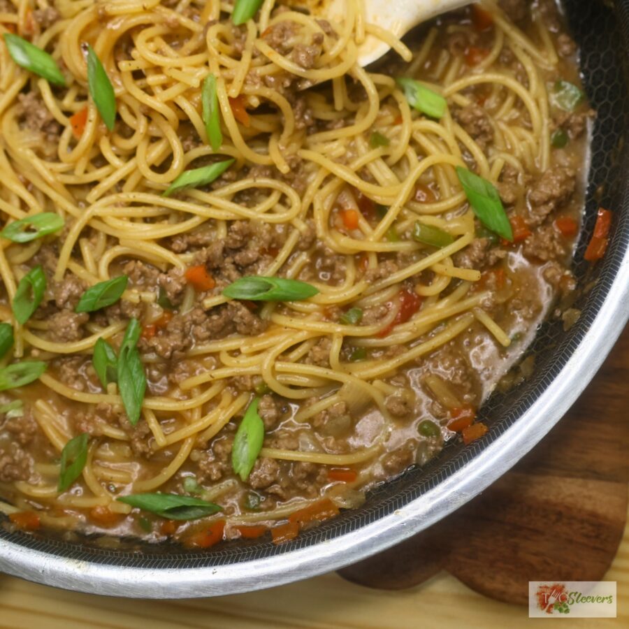 Close up image of dirty spaghetti in a skillet garnished with green onion