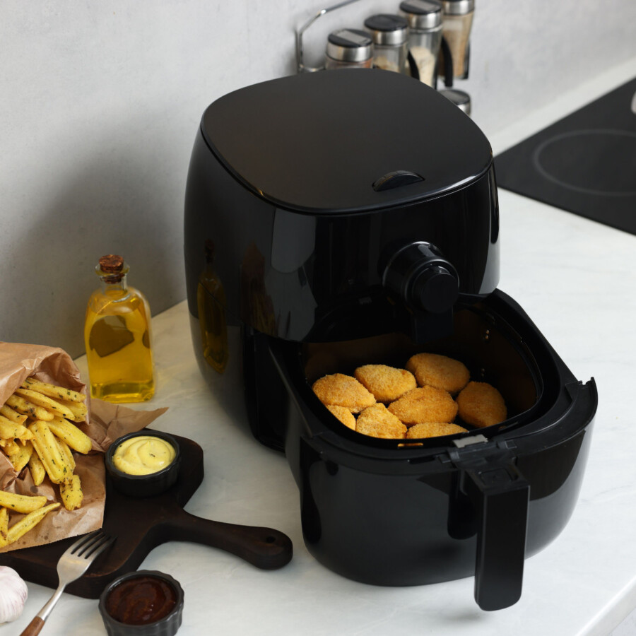 An air fryer with chicken nuggets on a white coutner top