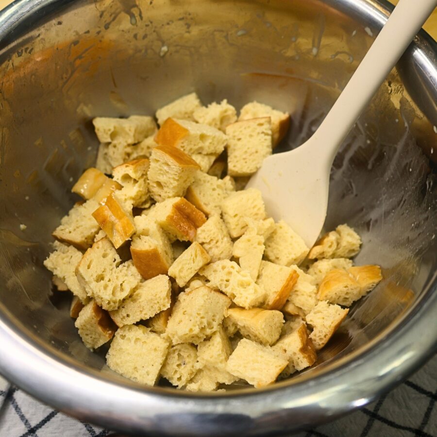 Cubed bread soaking in custard in a metal bowl