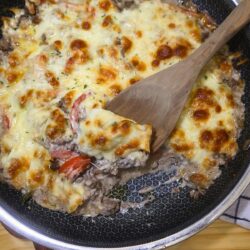 Ground Beef Cheesesteak Casserole in a skillet with a wooden spoon