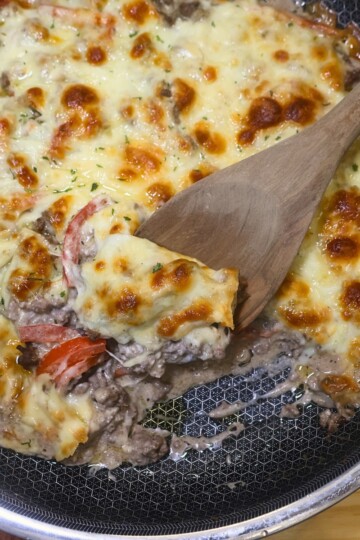 Ground Beef Cheesesteak Casserole in a skillet with a wooden spoon