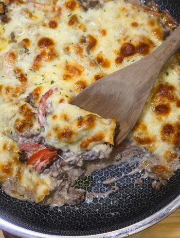 Ground Beef Cheesesteak Casserole in a skillet with a wooden spoon