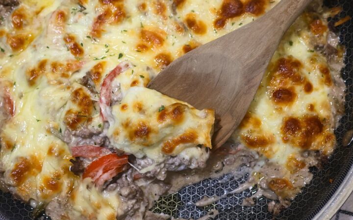 Ground Beef Cheesesteak Casserole in a skillet with a wooden spoon